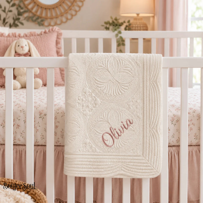 Personalized baby quilt featuring custom name embroidery in dusty rose script font on a premium scalloped ecru cream heirloom baby blanket.