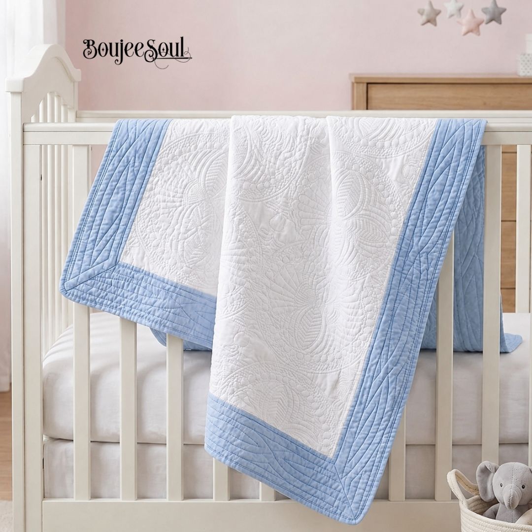 White and light blue personalized heirloom baby quilt by Boujee Soul, featuring a scalloped quilted trim, draped over a white wooden crib in a luxury baby boy nursery setting.